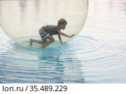 Little boy have fun inside big plastic balloon on the water of swimming pool on the summer resort. Kid inside big inflatable transparent ball running and having fun. Стоковое фото, фотограф Nataliia Zhekova / Фотобанк Лори