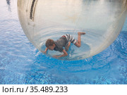 Little boy have fun inside big plastic balloon on the water of swimming pool on the summer resort. Kid inside big inflatable transparent ball running and having fun. Стоковое фото, фотограф Nataliia Zhekova / Фотобанк Лори
