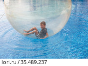 Little boy have fun inside big plastic balloon on the water of swimming pool on the summer resort. Kid inside big inflatable transparent ball running and having fun. Стоковое фото, фотограф Nataliia Zhekova / Фотобанк Лори