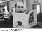 Мужчина средних лет сидит в помещении ресторана, пьёт пиво и читает меню с названием заведения "U kalicha", Чехословакия, 1960-е годы. Редакционное фото, фотограф Варфоломей Тетерин / Фотобанк Лори