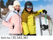 Girl and man in winterwear holding snowboard, looking at camera, winter resort with sunny day. Стоковое фото, фотограф Кекяляйнен Андрей / Фотобанк Лори