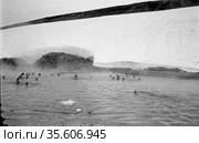 Большое количество детей школьного возраста купаются в ледяном водоёме, люди плавают рядом с ледником, пар поднимается из реки в воздух, Чукотка, 1970 год. Редакционное фото, фотограф Варфоломей Тетерин / Фотобанк Лори