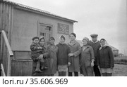 Коллективный фотопортрет людей позирующих стоя рядом с деревенским домом, одна из женщин держит ребёнка на руках, сельские жители, Лорино, Чукотка, 1970 год, колхоз Ленина. Редакционное фото, фотограф Варфоломей Тетерин / Фотобанк Лори