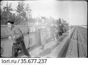 Молодые люди занимаются бегом на стадионе «Буревестник», они тренируются на деревянных трибунах под наблюдением тренера из Москвы, Якутия, апрель 1959 год. Редакционное фото, фотограф Варфоломей Тетерин / Фотобанк Лори