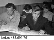 Ученики 9 класса вечерней школы сидят за школьными партами, они конспектируют информацию из учебников в тетради, мужчины и женщины молодого возраста получают среднее образование, Алдан, Якутия. Редакционное фото, фотограф Варфоломей Тетерин / Фотобанк Лори