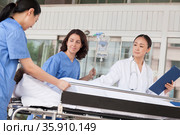 Female paramedics and doctor wheeling in a patient on a stretcher in front of the hospital. Стоковое фото, агентство Ingram Publishing / Фотобанк Лори
