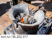 Кузнец держит кусок металла щипцами и нагревает его в печи. Печь с горящим углем. Мастер-класс по изготовлению сувениров из металла. Стоковое фото, фотограф Александр Бушков / Фотобанк Лори