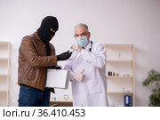 Masked man burglar bribing old doctor for getting vaccine. Стоковое фото, фотограф Elnur / Фотобанк Лори
