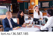 smiling female waiter bringing order to group of friens in restaurante. Стоковое фото, фотограф Яков Филимонов / Фотобанк Лори