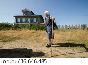 Пурнема. Старая женщина на фоне деревенского дома. Россия, Архангельская область, Онежский район (2021 год). Редакционное фото, фотограф Яковлев Сергей / Фотобанк Лори