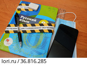 Учебник русского языка, школьные принадлежности, медицинская маска, смартфон и оградительная лента с надписью "дистанционное обучение" (2021 год). Редакционное фото, фотограф Цибаев Алексей / Фотобанк Лори