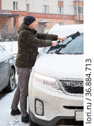 Male driver removes snow from the front of his snowy car, sweeping from the glass of windshield. Стоковое фото, фотограф Кекяляйнен Андрей / Фотобанк Лори