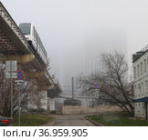 Москва, поезд монорельсовой транспортной системы движется по эстакаде вблизи станции Улица Милашенкова. Здания по другую сторону монорельсовой дороги теряются в тумане (2021 год). Стоковое фото, фотограф Наталья Николаева / Фотобанк Лори