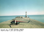 Гражданский вертолет на землях мыса Дежнёва, белый Маяк и люди на дальнем плане, земли омываются водами Берингова пролива, ясная погода, Чукотка, 1970. Стоковое фото, фотограф Варфоломей Тетерин / Фотобанк Лори