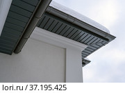 Corner of the house with new gray metal tile roof and rain gutter covered by snow at winter. Metallic Guttering System, Guttering and Drainage Pipe Exterior. Стоковое фото, фотограф Данила Большаков / Фотобанк Лори