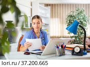 Young woman doctor studies the patient's outpatient card while sitting at a computer in the office. Стоковое фото, фотограф Яков Филимонов / Фотобанк Лори