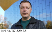 Businessman standing outdoors with office building in background, looking at camera and talking. Стоковое видео, видеограф Данила Большаков / Фотобанк Лори