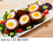 Tasty scotch eggs served with greens, leek and tomatoes at plate. Стоковое фото, фотограф Яков Филимонов / Фотобанк Лори