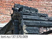 Close-up view of a burnt wooden house corner against a red brick wall. Стоковое фото, фотограф Игорь Мальцев / Фотобанк Лори