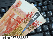 Черная пластиковая карта платежной системы "МИР" лежит между пятитысячных купюр на клавиатуре (2022 год). Редакционное фото, фотограф Цибаев Алексей / Фотобанк Лори