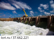 Kok-aral, Kazakhstan - May 03, 2012: Small Aral Sea Kok-aral dam. Water discharge in flood. Open shutters. Yellow mobile crane and workers on dam. Стоковое фото, фотограф Alexey Rezvykh / Фотобанк Лори