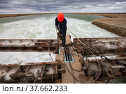 Kok-aral, Kazakhstan - May 03, 2012: Small Aral Sea Kok-aral dam. Worker in orange hardhat use steel rope to lifting water shutter weighting agent. Стоковое фото, фотограф Alexey Rezvykh / Фотобанк Лори