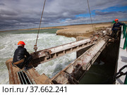 Kok-aral, Kazakhstan - May 03, 2012: Small Aral Sea Kok-aral dam. Two workers in orange helmets. Hoist water shutter weighting agent (steel girder) by crane. Редакционное фото, фотограф Alexey Rezvykh / Фотобанк Лори