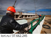Kok-aral, Kazakhstan - May 03, 2012: Small Aral Sea Kok-aral dam. Two workers in orange helmets hoist water shutter weighting agent (steel girder) by crane. Редакционное фото, фотограф Alexey Rezvykh / Фотобанк Лори