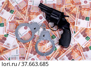Наручники и пистолет, лежащие на деньгах, крупным планом. Фон из российских рублей. Стоковое фото, фотограф Владимир Ходатаев / Фотобанк Лори