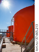 Orange steel storage tanks with acid and metal stairway on sulfuric (sulphuric) acid plant warehouse. Blue sky and sun background. Vertical photo. Стоковое фото, фотограф Alexey Rezvykh / Фотобанк Лори