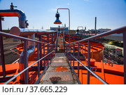 Orange steel storage tanks with acid at sulfuric (sulphuric) acid plant warehouse. Grid floor on the roof and lamp on blue sky. Стоковое фото, фотограф Alexey Rezvykh / Фотобанк Лори