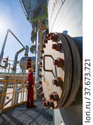 Aktobe region/Kazakhstan - May 04 2012: Oil refinery plant. Technician in red work wear and yellow helmet on refining column. CNPC company. Редакционное фото, фотограф Alexey Rezvykh / Фотобанк Лори