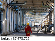 Aktobe region/Kazakhstan - May 04 2012: Refinery worker in red work wear and yellow helmet under the pipelines. Oil refinery plant. CNPC-AMG company. Редакционное фото, фотограф Alexey Rezvykh / Фотобанк Лори