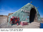 Khromtau, Aktobe region, Kazakhstan - May 06 2012: Gold ore mine portal. Title: Quarry (left) and Mechel company logo (right). Red firefighter tools and fire sand box. Blue sky and desert. Редакционное фото, фотограф Alexey Rezvykh / Фотобанк Лори