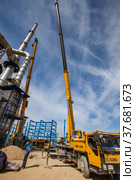 Aktau, Kazakhstan - May 19, 2012: Construction of asphaltic bitumen plant refinery column. Grey distillation tower, workers and yellow mobile crane (hydraulic hoist). Редакционное фото, фотограф Alexey Rezvykh / Фотобанк Лори