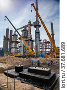Aktau, Kazakhstan - May 19, 2012: Construction of asphaltic bitumen plant. Grey distillation towers complex and yellow hydraulic hoist cranes. Редакционное фото, фотограф Alexey Rezvykh / Фотобанк Лори