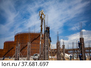 Aktau, Kazakhstan - May 19, 2012 Construction of modern asphaltic bitumen plant. Rusty oil storage tank. Making building columns. Workers on form. Rusty storage tank and blue sky with clouds. Стоковое фото, фотограф Alexey Rezvykh / Фотобанк Лори