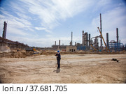 Aktau, Kazakhstan - May 19, 2012 Construction of modern asphaltic bitumen plant. Worker in balaclava mask with steel rope on sand. Refinery plant on background right, truck and pipeline left. Стоковое фото, фотограф Alexey Rezvykh / Фотобанк Лори