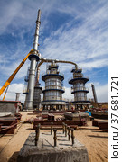 Aktau, Kazakhstan - May 19, 2012: Construction of asphaltic bitumen plant refinery column. Metal distillation tower and yellow hydraulic hoist. Редакционное фото, фотограф Alexey Rezvykh / Фотобанк Лори