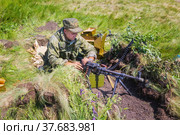 Russia, Samara, June 2019: A soldier in military uniform sits in ambush with a machine gun on a sunny summer day. Редакционное фото, фотограф Акиньшин Владимир / Фотобанк Лори