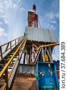 Uralsk region, Kazakhstan - May 24 2012: Oil deposit Zhaikmunai. Oil drilling rig and rusted drilling pipes and stair. Control panel with yellow valves right. Blue sky with clouds. Стоковое фото, фотограф Alexey Rezvykh / Фотобанк Лори
