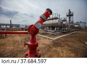 Uralsk region, Kazakhstan - May 24 2012: Oil deposit Zhaikmunai. Oil refinery plant. Fire extinguisher. Blurred heat exchanger, distilling tower, pipes on blue sky backgd. Focus on front. Редакционное фото, фотограф Alexey Rezvykh / Фотобанк Лори