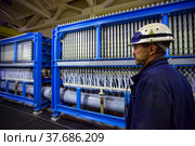 Pavlodar, Kazakhstan - May 29 2012: Caustic chemical plant. Chemical engineer in white hardhat and blue workwear and blue protective glasses on electrolytic process machine background. Редакционное фото, фотограф Alexey Rezvykh / Фотобанк Лори