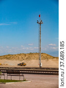 Khorgos, Kazakhstan-June 05, 2012: Railroad station in desert. Lighting mast, red flag on top.Rails and tractor on front,Heaps of sand and blue sky with light clouds on backdrop. Стоковое фото, фотограф Alexey Rezvykh / Фотобанк Лори