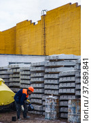 Temirtau, Kazakhstan - June 09, 2012: Concrete sleepers manufacturing plant NORD Prom NS outdoor warehouse. Worker marking sleepers. Yellow industrial building on background. Редакционное фото, фотограф Alexey Rezvykh / Фотобанк Лори