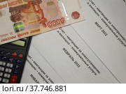 Квитанции за электроэнергию, крупная денежная купюра достоинством 5 тысяч рублей, калькулятор лежат на столе, вид сверху. Стоковое фото, фотограф Ольга Козловская / Фотобанк Лори