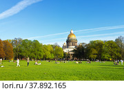 SAINT PETERSBURG, RUSSIA - May 13, 2018: People rest on a green lawn at Senatskaya Square against the background of St. Isaac's Cathedral on a warm day. Comfortable urban environment concept. Редакционное фото, фотограф Виктория Катьянова / Фотобанк Лори