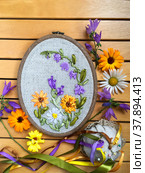 Hand embroidery with satin ribbons of a floral ornament with flowers of calendula, bluebells and daisies on a wooden background (embroidery was made by the author of the photo). Flat lay, closeup. Стоковое фото, фотограф Виктория Катьянова / Фотобанк Лори
