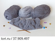 Knitting a warm gray scarf from wool and mohair yarn with bulky knitted braids. The row counter is worn on a knitting needle. Skeins of yarn on a white background. Winter handicraft and hobby. Стоковое фото, фотограф Виктория Катьянова / Фотобанк Лори