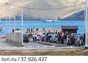 SAKHYURTA VILLAGE, MRS, BAIKAL LAKE, IRKUTSK REGION, RUSSIA - July 09, 2022: Autotourists stand in line for a ferry crossing to Olkhon Island - a favorite summer vacation spot. Редакционное фото, фотограф Виктория Катьянова / Фотобанк Лори